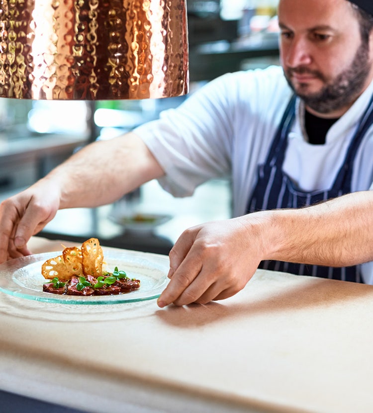 Chef placing a plate of food on a service counter at an Avendra International hotel, hospitality supplies
