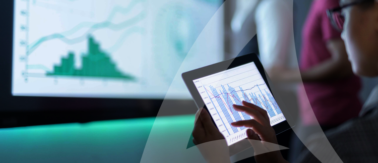 A person using a tablet to analyze data, with a larger screen displaying a bar graph in the background. A scene depicting technology and data visualization.