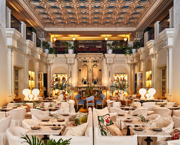 An elegant restaurant with plush seating, ornate columns, a grand fireplace, and high ceilings, creating a luxurious dining atmosphere.