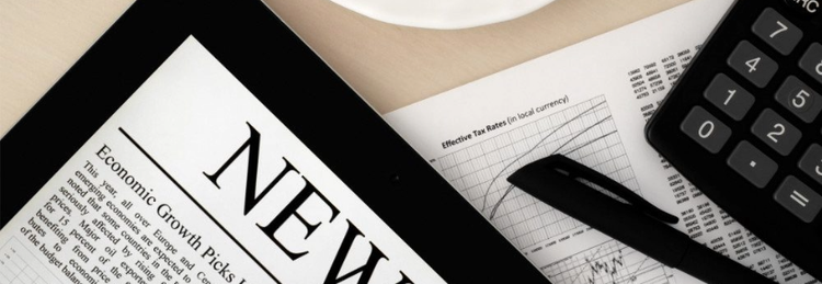 A tablet displaying a news article, placed on a desk alongside financial documents, a black pen, a calculator, and a white coffee cup on a saucer