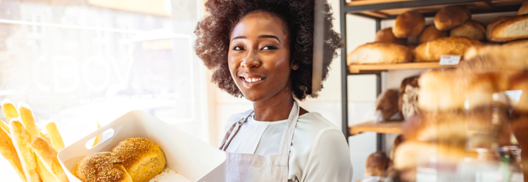 Woman who works at a bakery smiling and holding loaves of bread