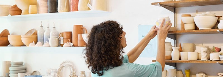 Woman holding pottery dish near shelves filled with pottery