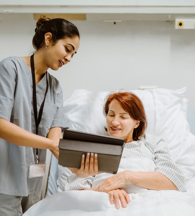 Smiling nurse showing a digital tablet to a senior patient in a hospital, promoting Avendra International's innovative healthcare procurement services and electronic meal ordering solutions.