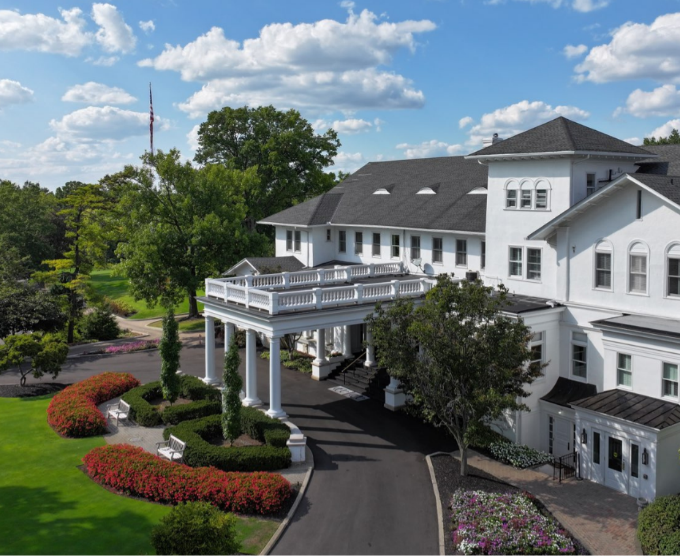 A grand white building with a columned entrance, dark gray roof, and a manicured garden, exuding a stately and official presence.