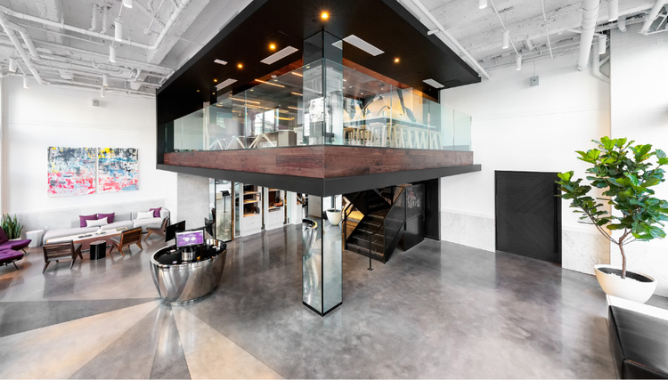 A modern lobby with a sleek reception desk, stylish seating, and open staircase.