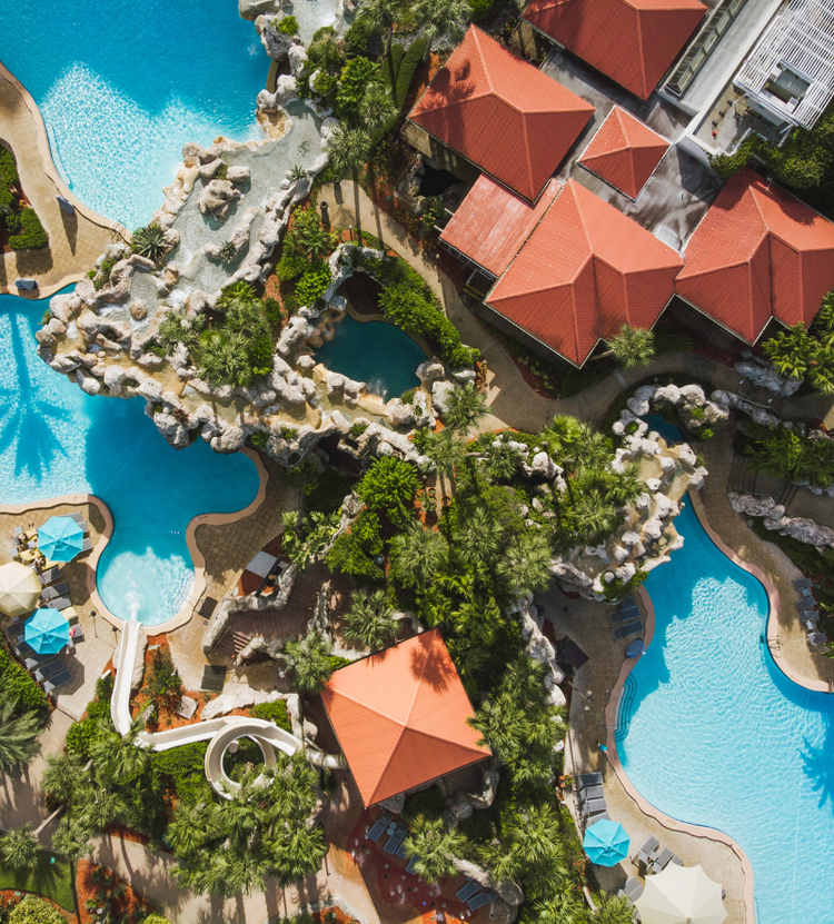 An aerial view of a resort featuring multiple swimming pools, water slides, red-roofed buildings, and lush greenery, designed for relaxation and recreation.