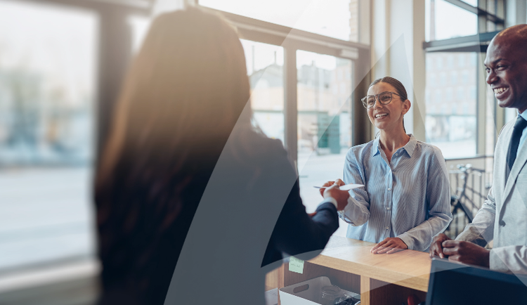 People exchanging an item over a countertop with large windows in the background