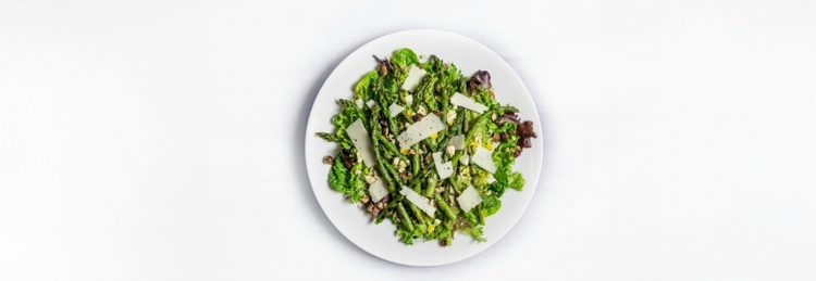Une assiette blanche avec une salade verte fraîche, composée d'asperges, de légumes verts mélangés et de fromage.