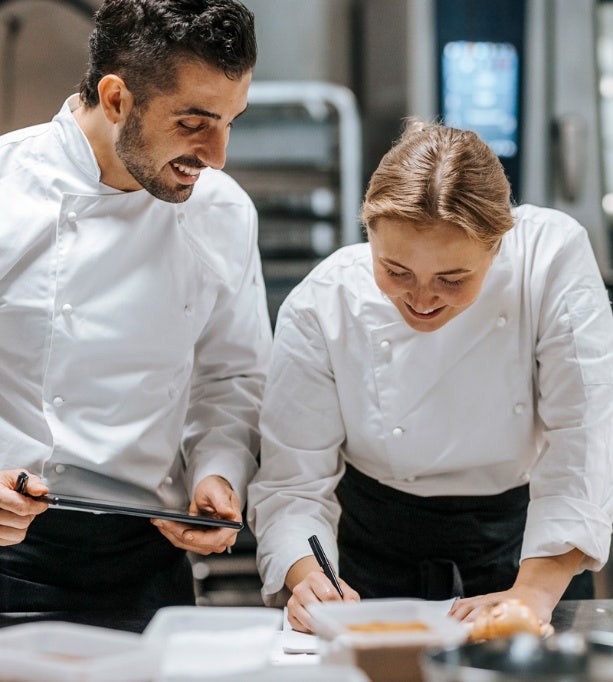 Des chefs hommes et femmes heureux font de la comptabilité dans la cuisine d'un restaurant, mettant en valeur les services culinaires et d'assistance au menu d'Avendra International.