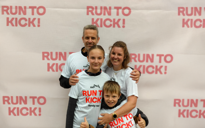 Une famille posant devant une bannière de l'événement Run To Kick.