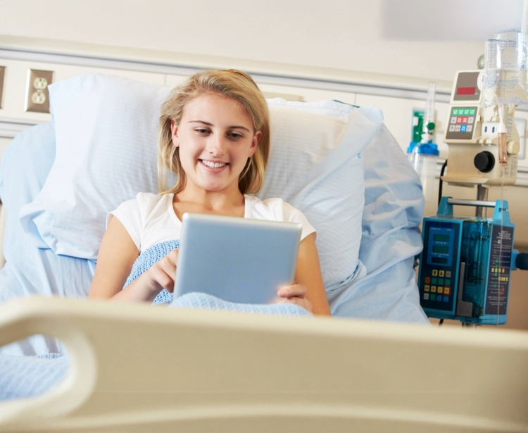 Une femme souriante dans un lit d'hôpital, utilisant une table.