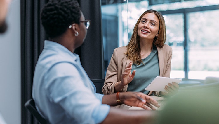 Une femme discutant avec un collègue, une tablette à la main.