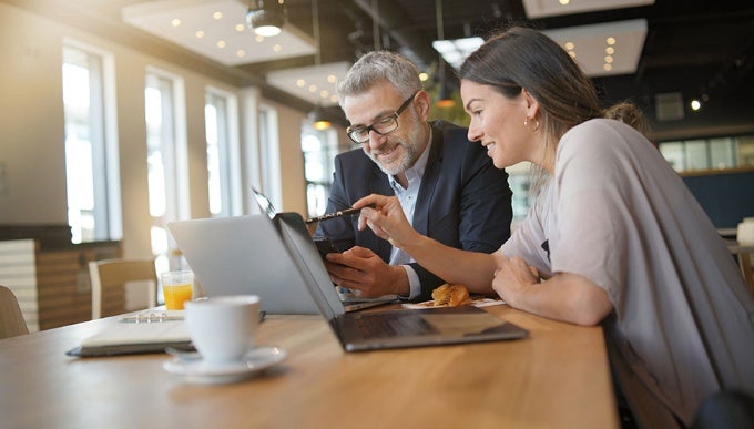 Een man en een vrouw werken op hun laptops in een helder verlicht café.