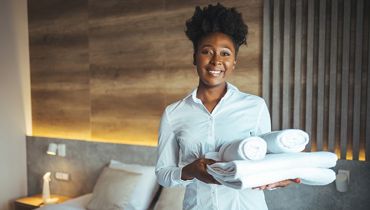 Hotelpersoneel poseert met een stapel witte handdoeken in een hotelkamer.