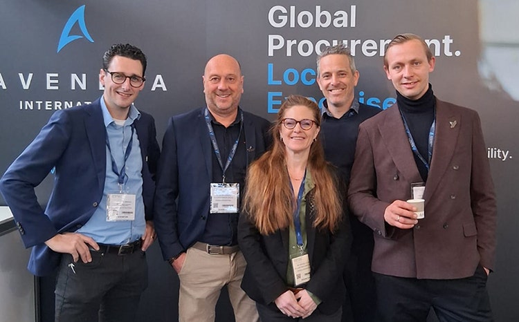 Een groep professionals poseert voor een achtergrond met het logo van Avendra International.