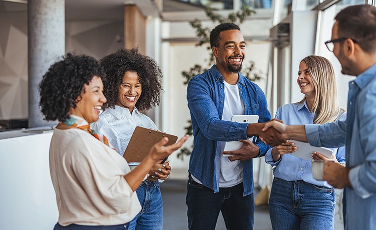 A group of colleagues engaging in a conversation. Two colleagues shake hands
