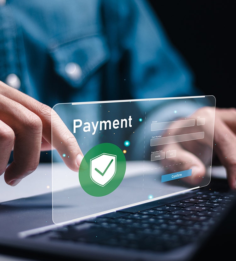 A person using a laptop while interacting with a transparent, futuristic payment interface displaying fields for payment details, including Owner, Card Number, Expiration Date, and CVV, with a green shield icon for security and a Confirm button.