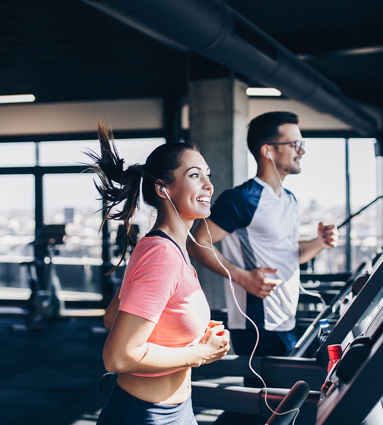 Man en vrouw rennen op loopbanden terwijl ze bedrade oortelefoons dragen.
